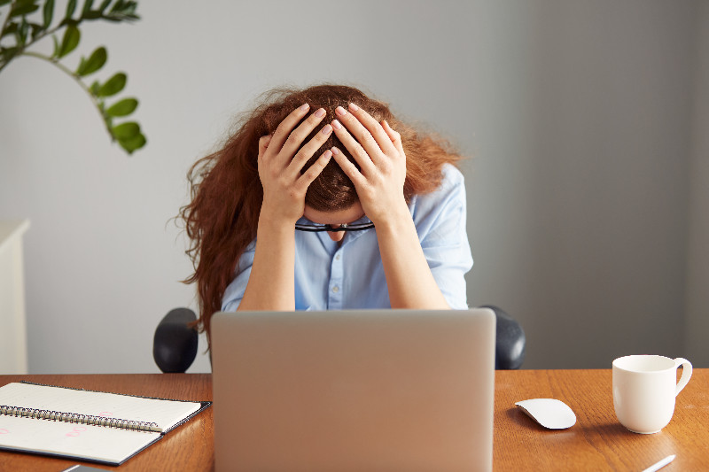 Frau sitzt am Schreibtisch vor dem Laptop und hält sich erschöpft ihren Kopf.