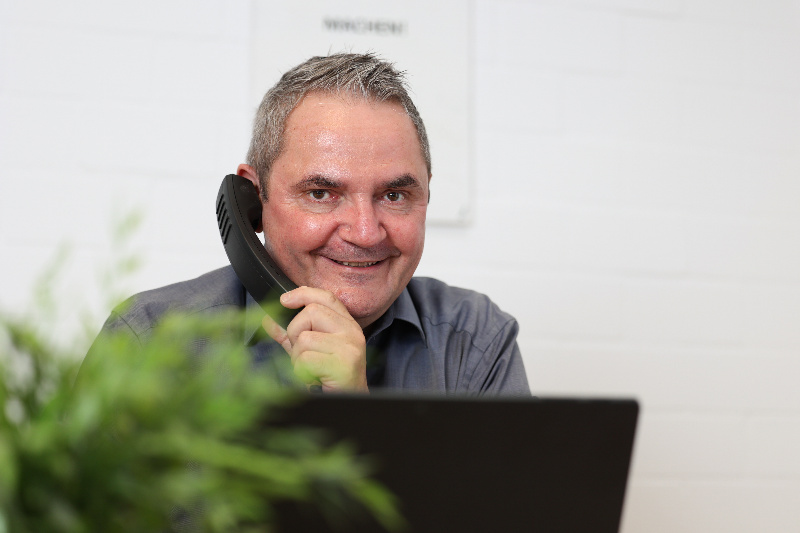Ulrich Liebscher telefoniert lächelnd im Büro am Laptop