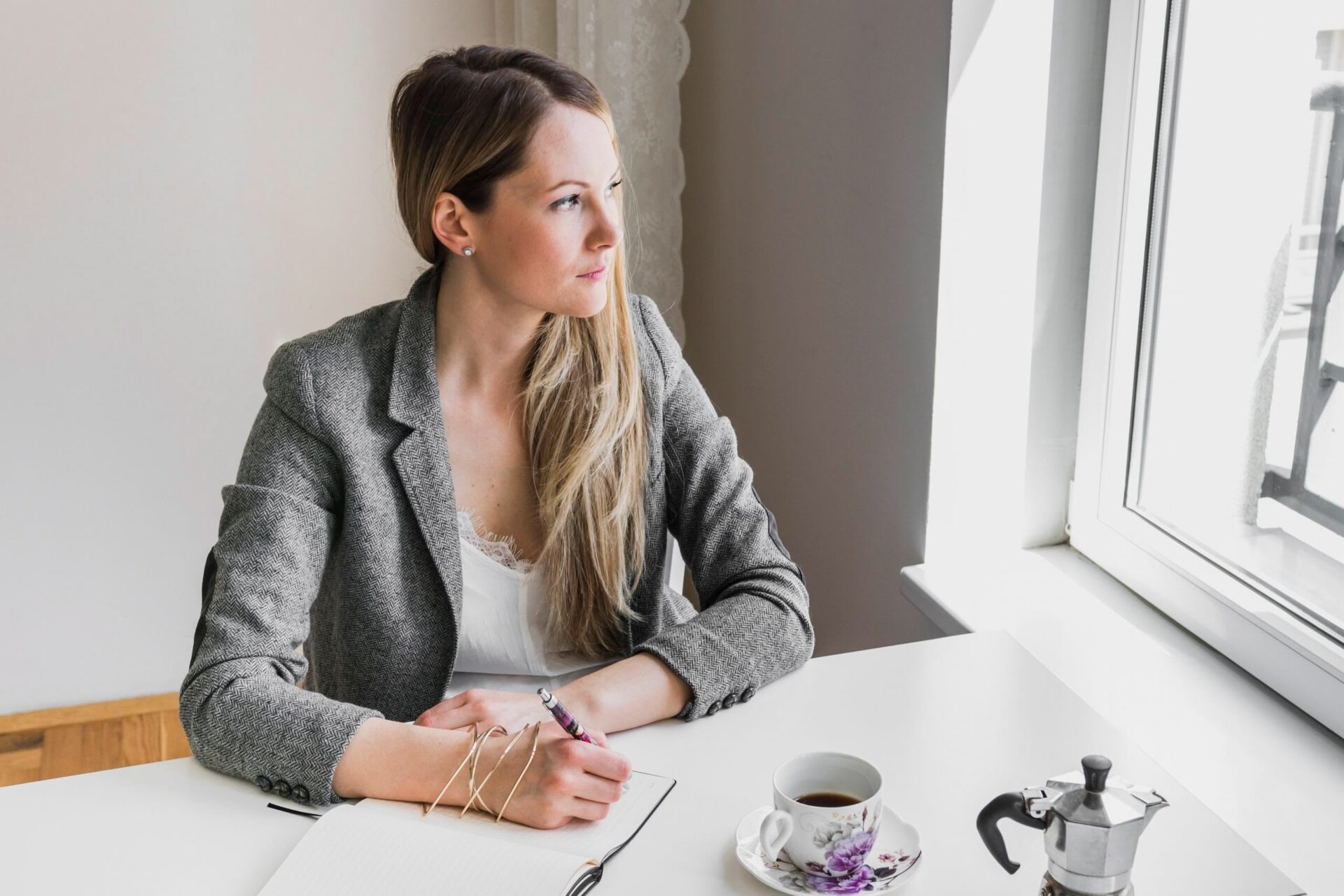 Frau schreibt in Notizbuch, schaut aus dem Fenster.