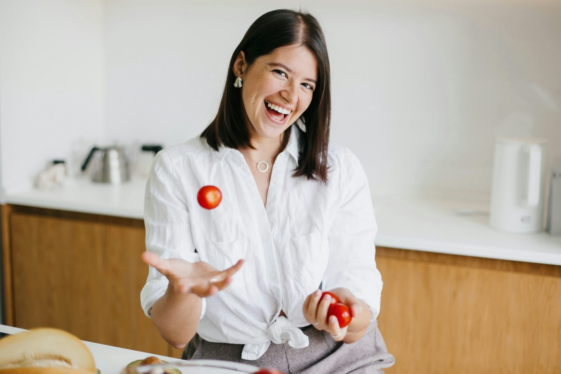 Frau jongliert in moderner Küche mit Tomaten.